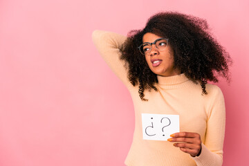 Young african american curly woman holding an interrogation on a placard touching back of head, thinking and making a choice.