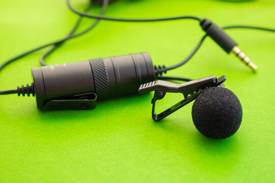 Professional lavalier or lapel microphone on a colored surface, very close-up. Details of the grip clip or fastener, mic power bank, Concept useful object, sound production, Video production.