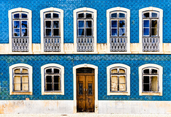 frontal view of a house facade covered in azulejo tiles with broken windows and wooden door