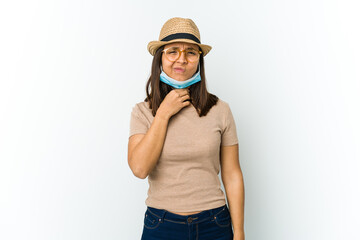 Young latin woman wearing hat and mask to protect from covid isolated on white background suffers pain in throat due a virus or infection.