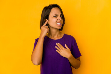 Young hispanic woman isolated on yellow covering ears with fingers, stressed and desperate by a loudly ambient.