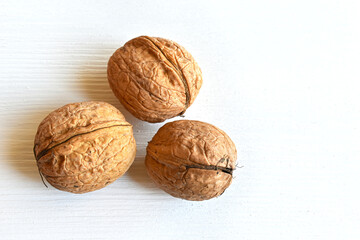 Walnuts (Juglans regia) in shell on white wooden background, close-up, top view.