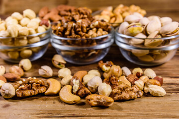 Various nuts (almond, cashew, hazelnut, pistachio, walnut) in glass bowls on a wooden table. Vegetarian meal. Healthy eating concept