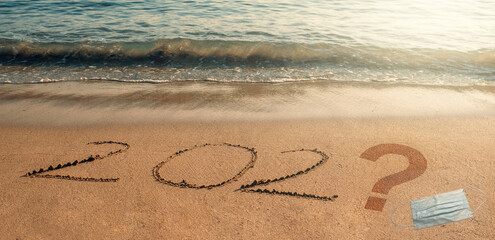 Text on sandy beach 202 question mark and face mask, concept of when and in what year coronavirus covid-19 will end.
