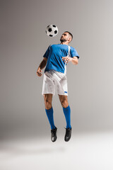 Fototapeta na wymiar Sportsman jumping near football while training on grey background