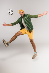 Positive man jumping near football in air on grey background