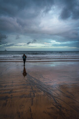 a girl with a blue backpack walking along a beach on a cloudy winter day