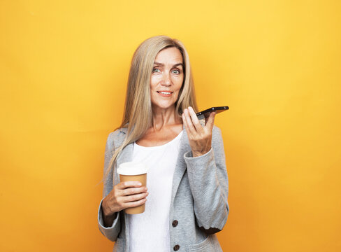 Attractive Smiling Mature Woman With Long Gray Hair Holding Mobile Phone And Cup Of Takeaway Coffee