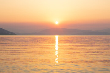 Sunrise / sunset over the sea, rocks and cliffs come out of the water with reflections of warm colors, golden hour.