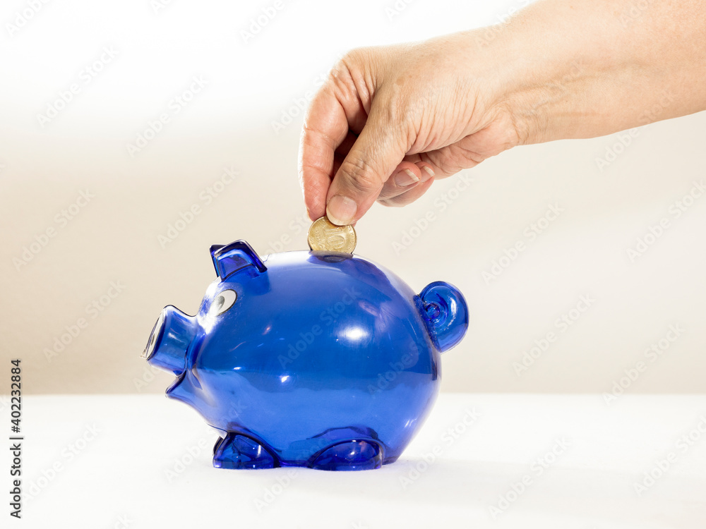 Wall mural woman's hand putting coin into a blue piggy bank. household