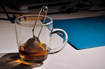 Stainless steel tea infuser in glass mug, cup of tea on a table. Half-finished, selective focus.