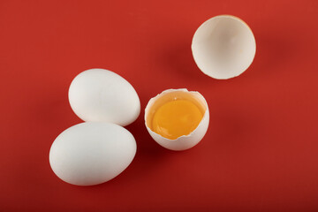 Broken and whole raw eggs on red background