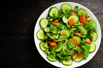 Salad with baby spinach, tomatoes, fresh arugula and cucumber on stoned background . Concept for a tasty and healthy meal.Vitamins in vegetables and herbs for immunity against the virus.Top view.