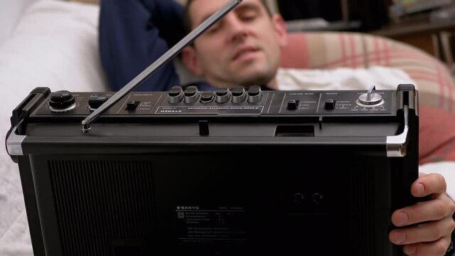 Tired Male Lying on Bed Presses Play Button on Old Cassette Radio with Antenna