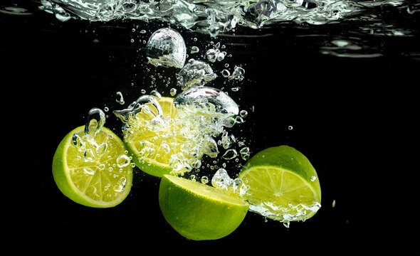 Lime Citrus Fruits splashing with bubbles into water isolated against black background. Citrus theme.
