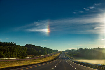 Fototapeta na wymiar A sun halo, or son dog, appearing during the early morning sunrise above a rural highway