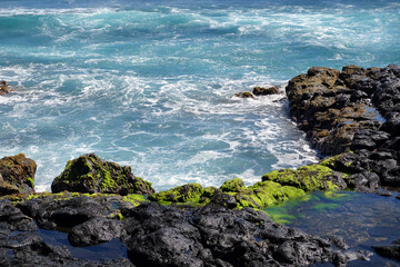 Beach near the Hanga Roa village on Easter Island, with blue waters surrounded by black volcanic rocks and green vegetation.