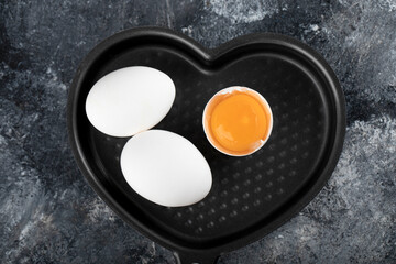 Two white eggs and yolk on heart shaped pan
