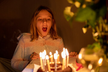 happy girl blowing out candles at her birthday eleven years old in lockdown, blurred face,...