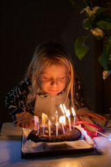 little girl blowing out candles with closed eyes at birthday party in lockdown in pajamas, blurred face, vertical