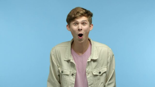 Slow motion of handsome guy raising eyebrows in surprise, hear great news and feeling happy for friend, congratulating, showing thumb up and praising you, standing over blue background