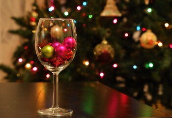 Christmas ornaments inside the champagne glass with bokeh soft blurred Christmas tree background 