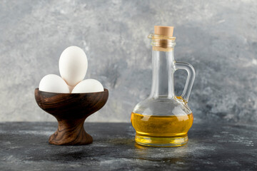 Bowl of white eggs and bottle of oil on marble background