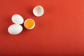 Broken and whole raw eggs on red background