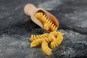 Wooden spoon of raw fusilli on marble background