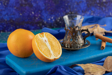 Glass of tea, orange and cinnamon sticks on blue board