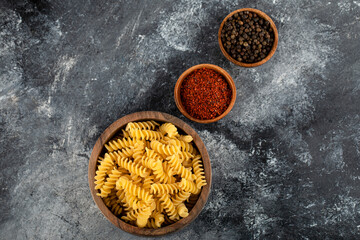 Raw fusilli pasta in wooden bowl with pepper spices