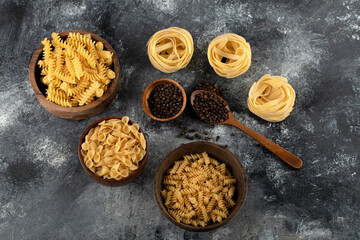 Dry pasta and black pepper grains on marble background