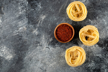 Dry tagliatelle nests and ground red pepper on marble background
