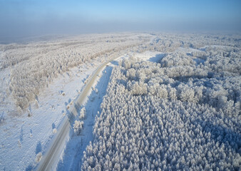 Aerial photo of winter road surrounded by birch forest.  Drone shot of trees covered with hoarfrost and snow.