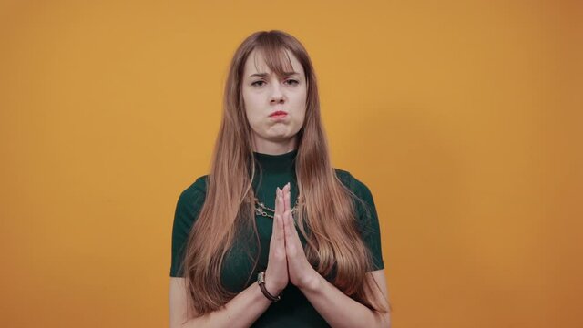 Folded hands together praying asking God for help ask implore wish upwards Jesus Christ. Young attractive woman, dressed green shirt blonde hair, yellow background