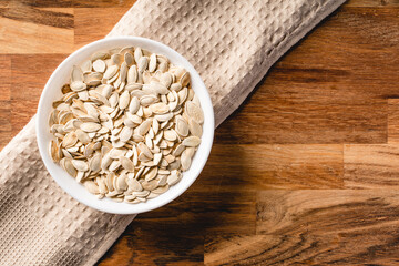 Top view on fresh salted roasted pumpkin seeds in bowl on wooden table at home