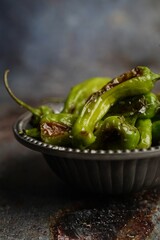 Blistered shishito peppers in a bowl on dark moody setting