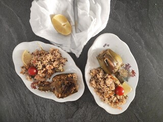 Two ocal plates of meal composed by artichoke, baked quinoa and cherry tomatoes