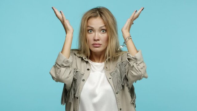 Slow motion of frustrated blond woman showing head explosion gesture, blowing head and staring shocked at camera, standing confused against blue background