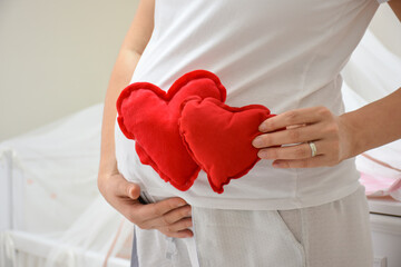 Pregnant woman holding a red heart sign. Pregnant woman put twins toy heart to her stomach on white background