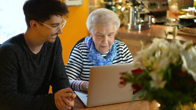 Overhead view of happy senior elderly woman sitting with teen grandson learning to use laptop computer in dining room.
