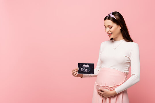  young pretty pregnant woman holding ultrasound scan isolated on pink