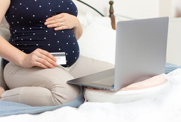 Naklejka premium Closeup of pregnant woman with big tummy use laptop to buy baby products and hold credit or debit card. Shopping online during quarantine. Concept of online pregnancy shopping. Mother waiting baby. 