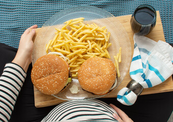 Cropped image of young hungry pregnant woman eating a hamburger and fried potatoes. Concept of...