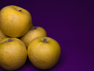 Alimentos saludables. Grupo de manzanas amarillas apiladas sobre un fondo de color púrpura con espacio para texto