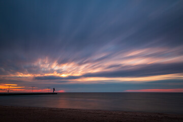 An early morning sunrise breaks through the fast-moving clouds as a lighthouse sits on the banks of Lake Ontario