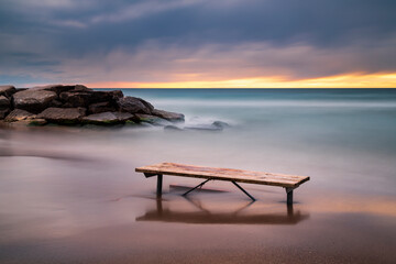 Long exposure of a picnic bench  on the rocky shores of Lake Ontario at sunrise