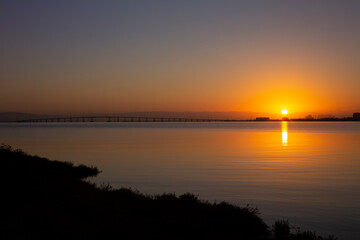 Naklejka premium End of a summer day on the San Francisco East Bay, Coyote Point, California. Brilliant sunset setting over the bay with silhouette of bay bridge