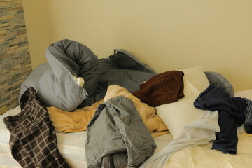 洋服が散らかった汚い部屋のベットと布団と枕
