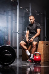 Fototapeta na wymiar Muscular athlete with weightlifting equipment. Trainer in a fitness studio. Smoke background.